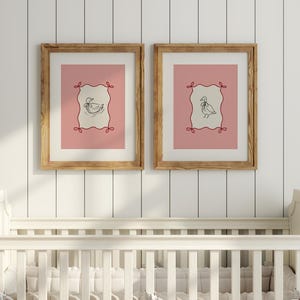 May include: Two framed prints with a pink and white striped background. Each print features a black and white illustration of a duck inside a red and white frame. The frames are made of wood and have a natural finish.