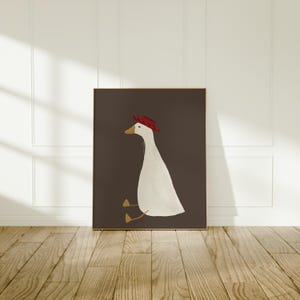 May include: A white goose wearing a red hat sits on a dark brown background. The goose is facing to the left and has its head tilted slightly to the right. The goose's feet are visible and are a light brown color.