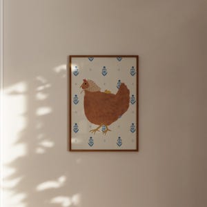 Puede incluir: Una ilustraci&oacute;n enmarcada de una gallina marr&oacute;n que lleva un gorro blanco con un pollito amarillo en la espalda. La gallina est&aacute; de pie sobre un fondo blanco con un patr&oacute;n floral azul y blanco.