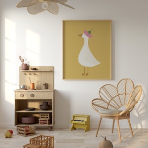 May include: A light wood play kitchen with a toy truck, a toy piano, and a wicker chair in a room with a white wall and a framed print of a goose wearing a pink flower on its head.