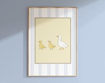 May include: A framed print featuring a whimsical illustration of a mother goose and two ducklings. The artwork is set against a pale yellow background, framed by a black border, and a striped pattern. The frame is a light wood color.