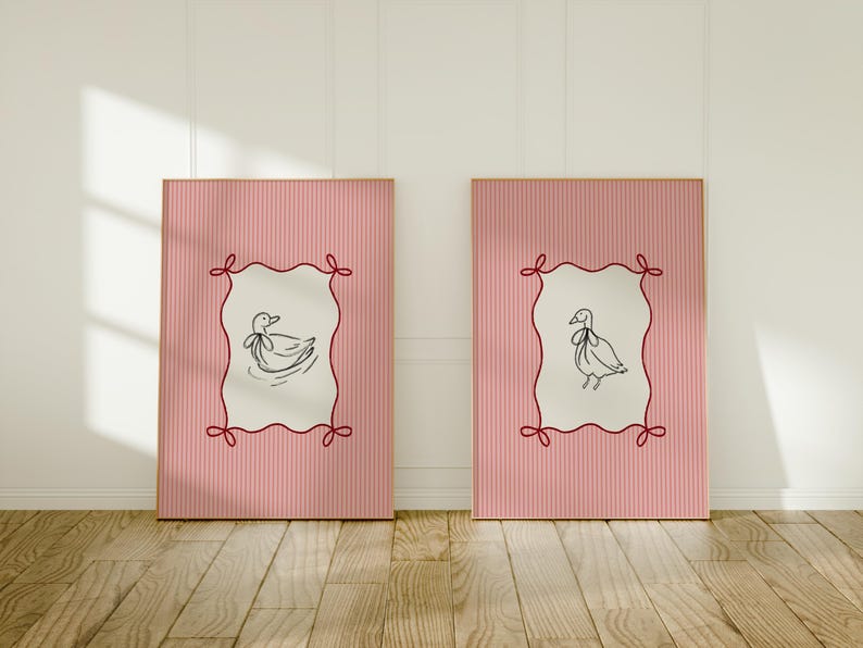 May include: Two pink framed prints with white backgrounds and red ribbon accents. Each print features a black and white line drawing of a duck with a ribbon around its neck.
