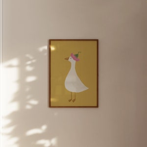 May include: A framed illustration of a white goose wearing a pink flower on its head. The goose is standing on a yellow background.