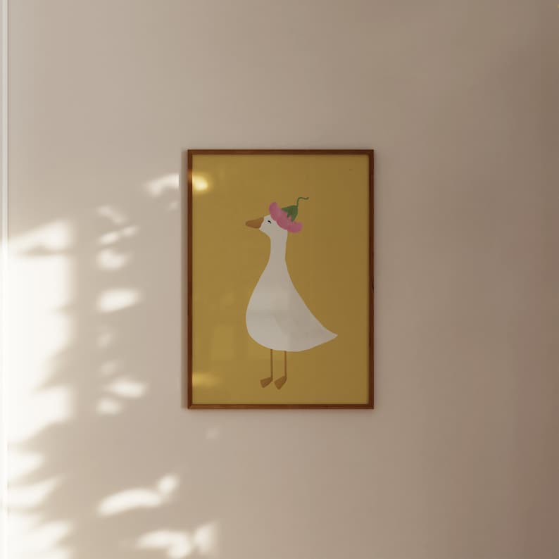 May include: A framed illustration of a white goose wearing a pink flower on its head. The goose is standing on a yellow background.