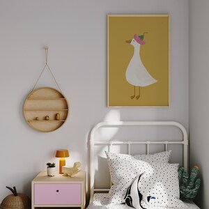 May include: A white single bed with a white metal frame and a white and black polka dot duvet cover. A white pillow with black polka dots and a black and white penguin pillow are on the bed. A green cactus plush toy is on the bed. A yellow lamp is on a pink nightstand next to the bed. A round wooden shelf with three shelves is hanging on the wall. A framed print of a white goose wearing a pink flower hat on a yellow background is hanging on the wall.