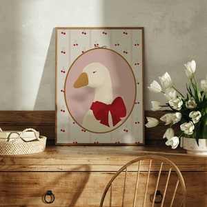 May include: A framed illustration of a white goose with a red bow, set against a pink background with a pattern of red cherries on a white and pink striped background.