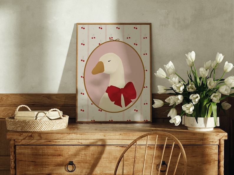 May include: A framed illustration of a white goose with a red bow, set against a pink background with a pattern of red cherries on a white and pink striped background.