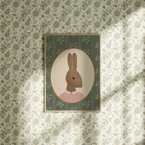 May include: A framed illustration of a brown rabbit wearing a pink shirt. The illustration is set against a green background with a white floral pattern.