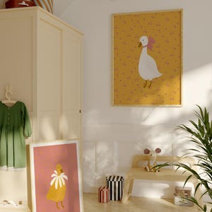 Pu&ograve; includere: Due illustrazioni incorniciate di oche con accenti floreali. L'illustrazione superiore presenta un'oca bianca con un fiocco rosa su uno sfondo giallo con punti rosa. L'illustrazione inferiore presenta un'oca gialla con un collare di fiori bianchi su uno sfondo rosa con punti gialli.