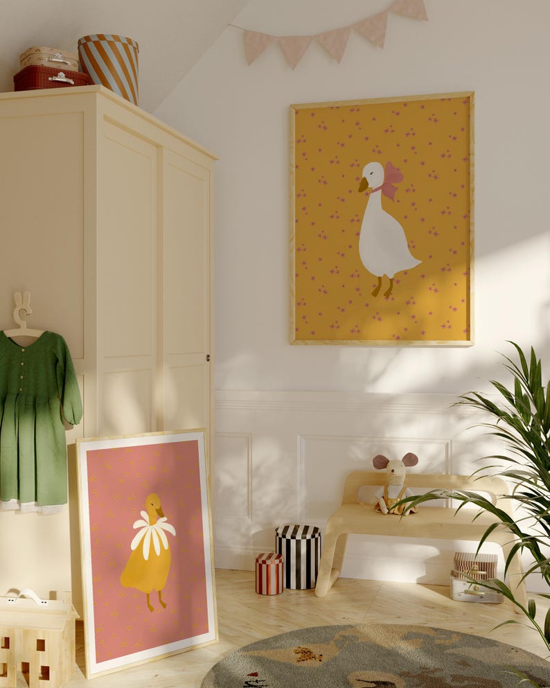 Pu&ograve; includere: Due illustrazioni incorniciate di oche con accenti floreali. L'illustrazione superiore presenta un'oca bianca con un fiocco rosa su uno sfondo giallo con punti rosa. L'illustrazione inferiore presenta un'oca gialla con un collare di fiori bianchi su uno sfondo rosa con punti gialli.