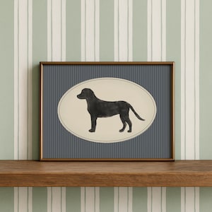 Può includere: Una stampa incorniciata con un'illustrazione di un Labrador Retriever nero. Il cane è raffigurato di profilo all'interno di una cornice ovale, su uno sfondo a strisce blu. La cornice è di colore marrone scuro e la stampa è esposta su una mensola di legno.
