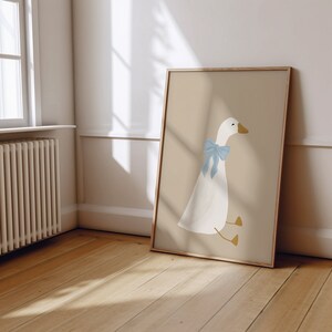 May include: A framed illustration of a white goose with a light blue bow sitting on a beige background.