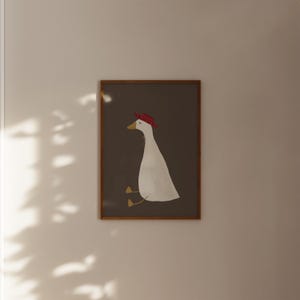 May include: A framed illustration of a white goose wearing a red hat, sitting on a brown background.