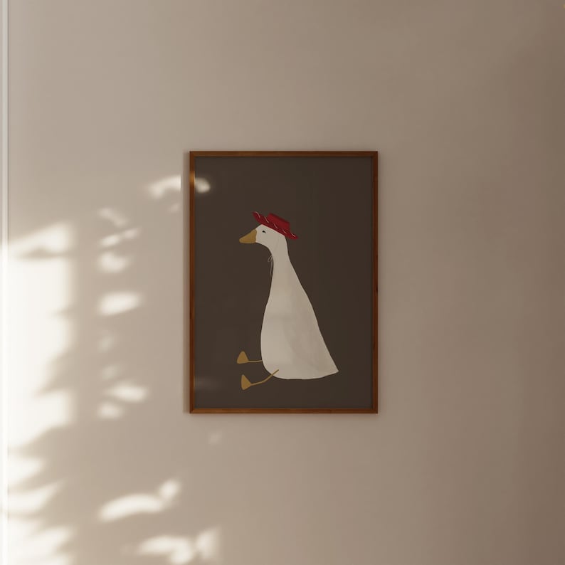 May include: A framed illustration of a white goose wearing a red hat, sitting on a brown background.
