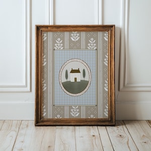 May include: A framed print with a light blue and white gingham pattern background. A white house with a brown roof is in the center of a green circle with a brown border. The circle is surrounded by a light blue and white gingham pattern.