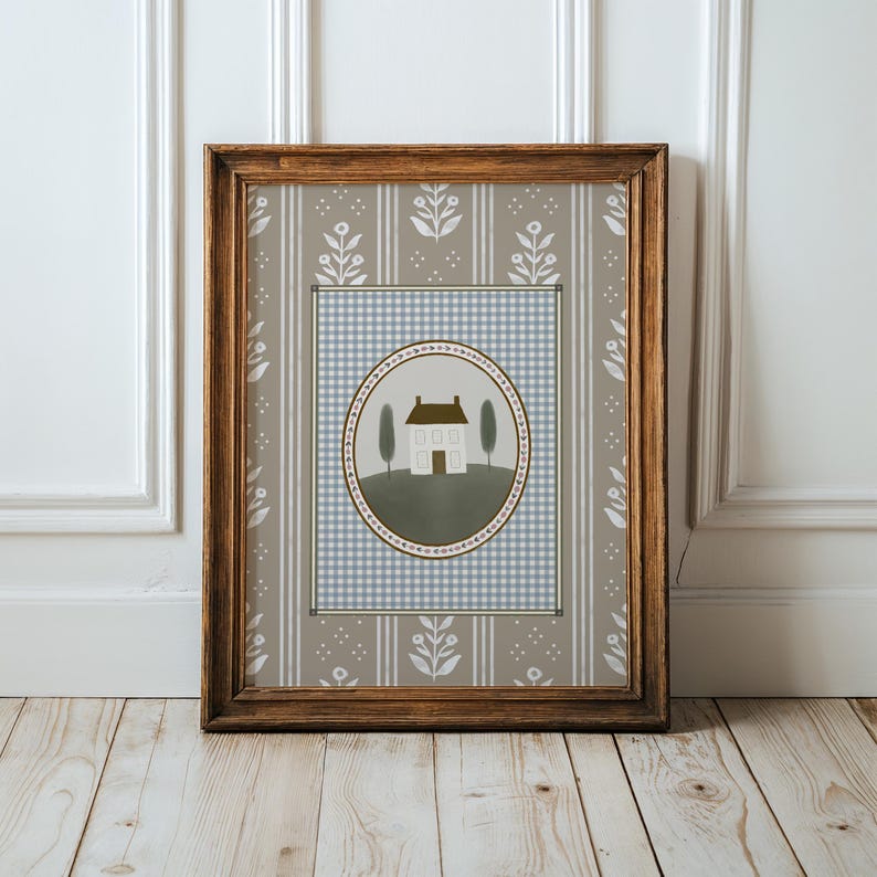May include: A framed print with a light blue and white gingham pattern background. A white house with a brown roof is in the center of a green circle with a brown border. The circle is surrounded by a light blue and white gingham pattern.