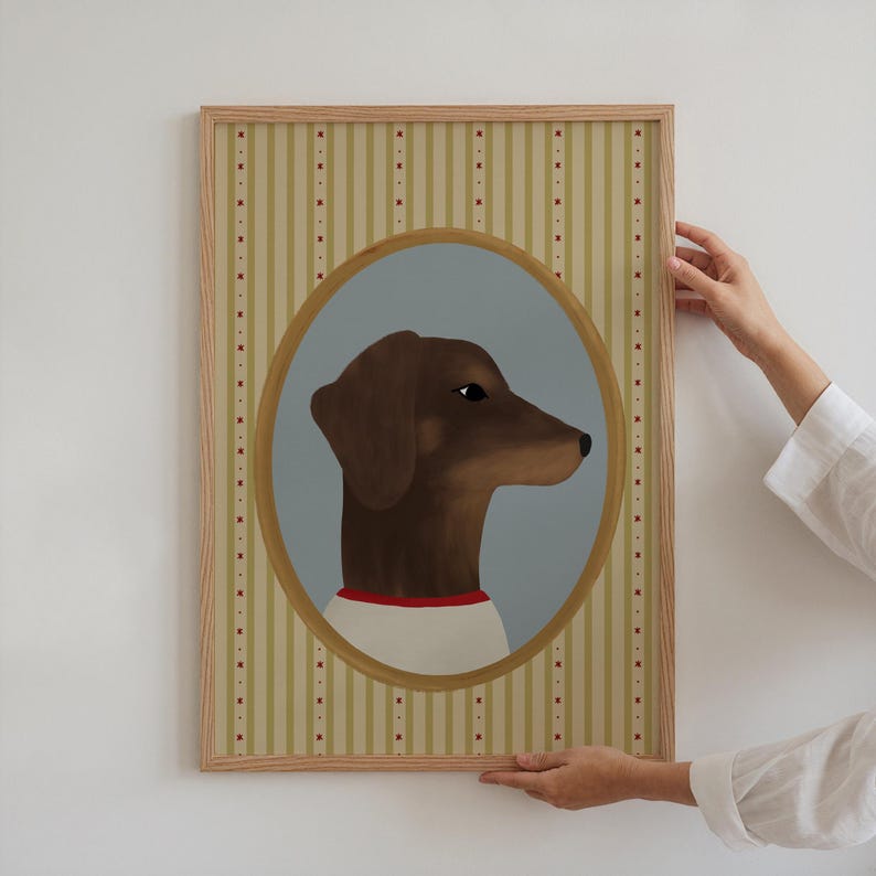 May include: A framed artwork featuring a brown dachshund dog in profile, set within an oval frame against a light blue backdrop. The dog wears a white shirt with a red collar. The frame has a striped background.