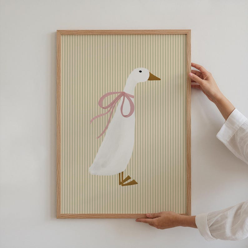 May include: A framed illustration of a white goose with a pink bow on a yellow and white striped background.