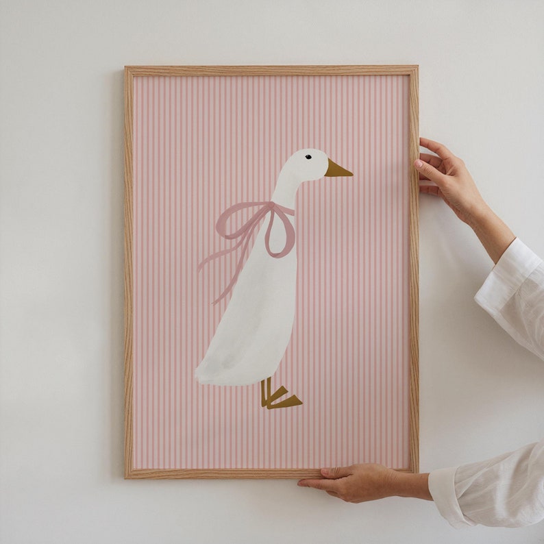 May include: A framed print of a white goose with a pink bow on a pink and white striped background.