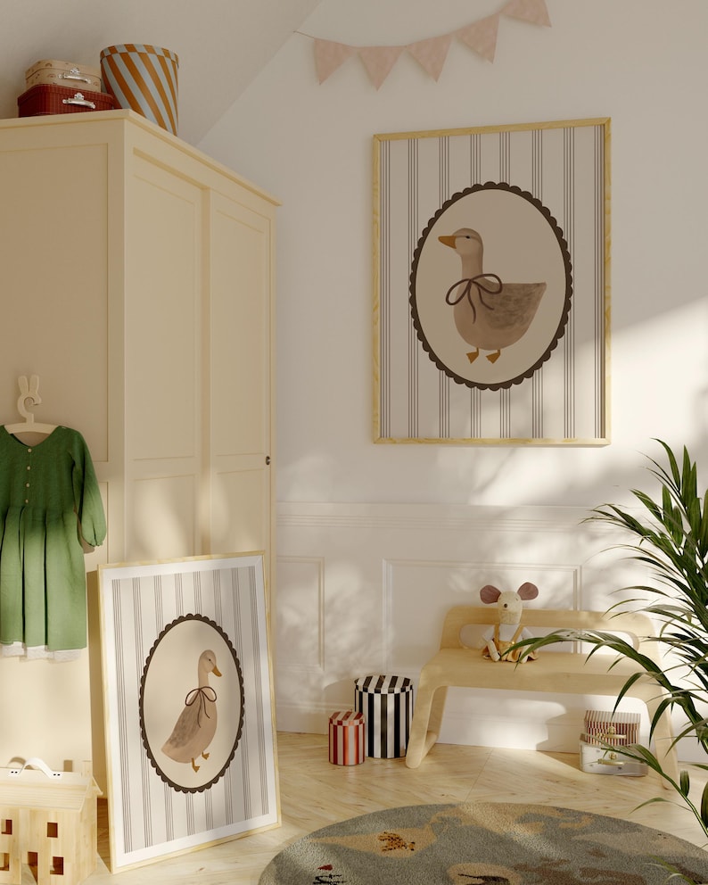 May include: Two framed prints of a brown duck with a brown bow on a white background with brown stripes. The prints are hanging on a white wall in a room with a wooden bench and a green plant.