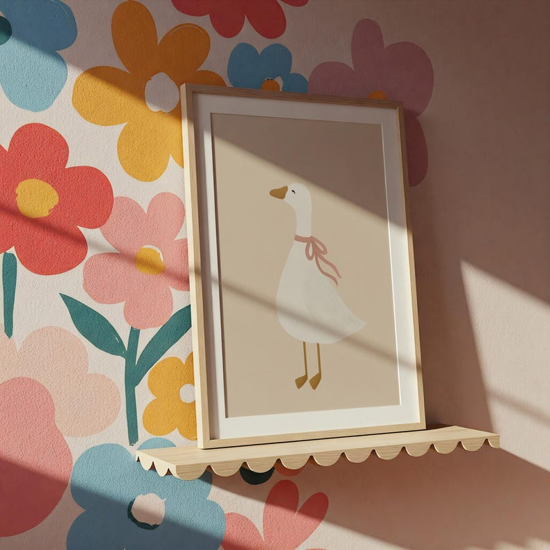 May include: A framed art print featuring a white goose with a pink ribbon around its neck. The artwork is displayed on a scalloped wooden shelf against a floral wallpaper background. The print has a beige background.