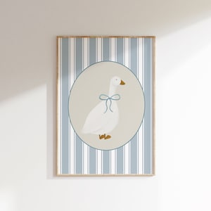 Könnte beinhalten: Eine weiße Gans mit einer blauen Schleife ist in einem Kreis auf einem blau-weiß gestreiften Hintergrund abgebildet. Die Gans blickt nach rechts und hat einen braunen Schnabel und Füße.
