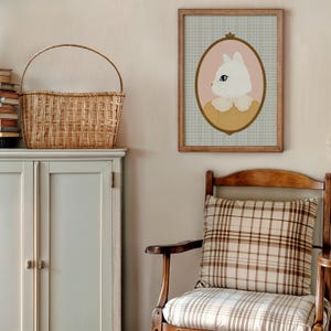 May include: A framed illustration of a white cat with a yellow collar, set against a pink oval and a blue and white checkered background. The frame is brown wood and the illustration is in a vintage style.