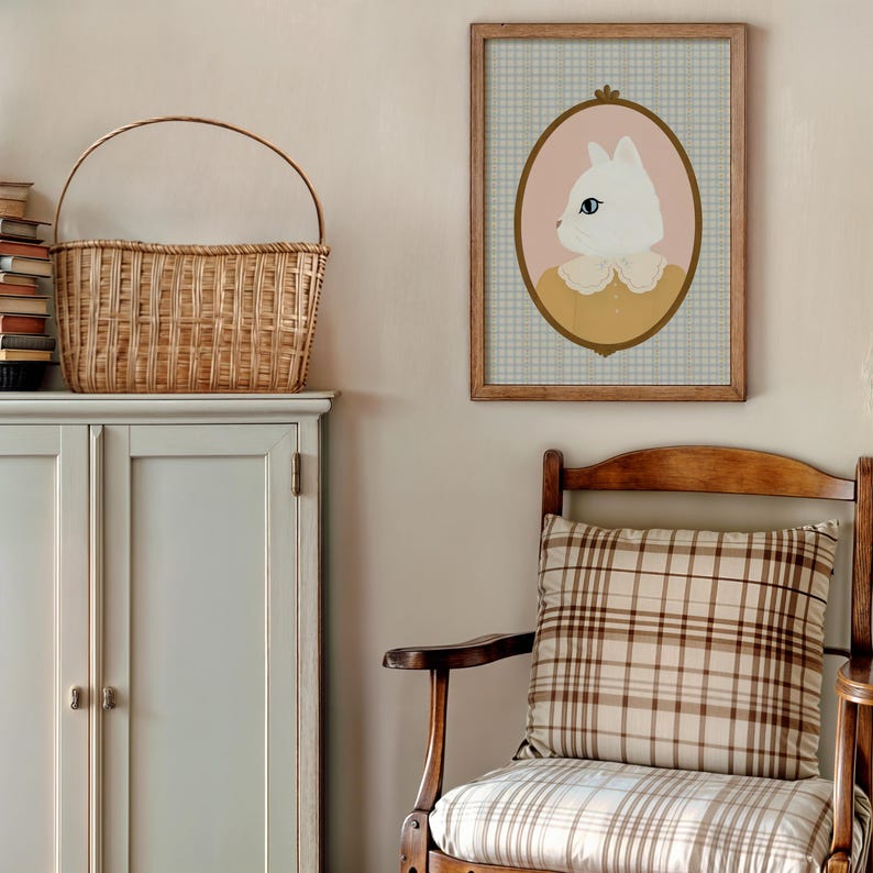 May include: A framed illustration of a white cat with a yellow collar, set against a pink oval and a blue and white checkered background. The frame is brown wood and the illustration is in a vintage style.