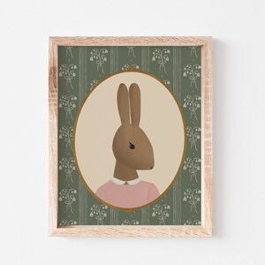 May include: A framed illustration of a brown rabbit wearing a pink shirt, set against a green background with a floral pattern.