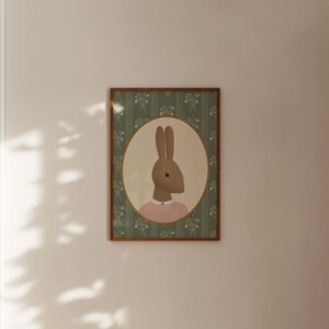 May include: A framed illustration of a brown rabbit wearing a pink dress, set against a green floral background.
