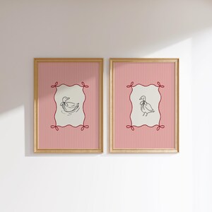 May include: Two framed prints with pink and white striped backgrounds. Each print features a black line drawing of a duck with a red ribbon around its neck inside a red, white, and cream colored frame.