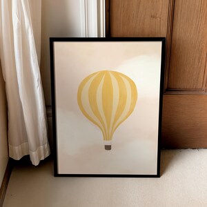 May include: A framed print of a yellow hot air balloon with white stripes against a light pink background.