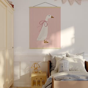 May include: A pink and white striped poster with a white goose wearing a pink bow. The poster is hanging on a white wall above a bed with a light blue blanket and a pillow with a house design.