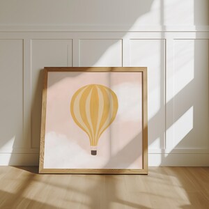 May include: A framed print of a yellow hot air balloon with white stripes against a pink background with white clouds.