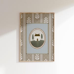 May include: A framed print with a light blue and white gingham pattern background. A white house with a brown roof is centered in a green oval with a pink and brown border. The oval is surrounded by a light blue and white gingham pattern. The frame has a brown and white floral pattern.