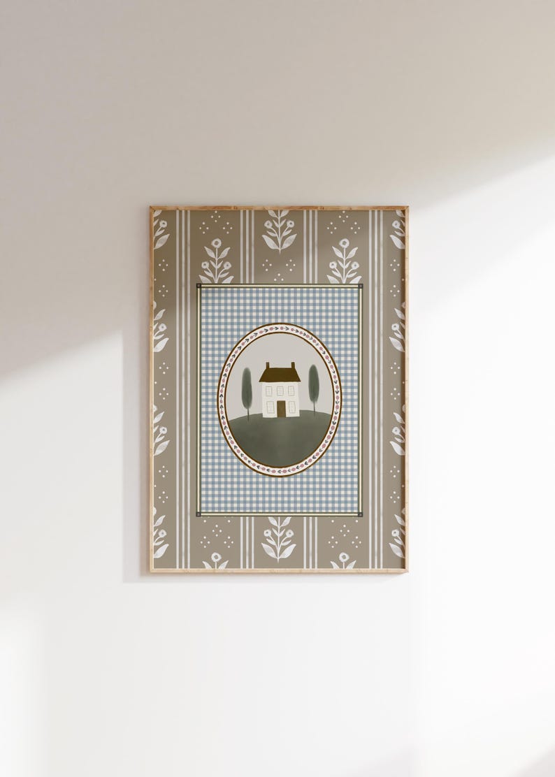 May include: A framed print with a light blue and white gingham pattern background. A white house with a brown roof is centered in a green oval with a pink and brown border. The oval is surrounded by a light blue and white gingham pattern. The frame has a brown and white floral pattern.