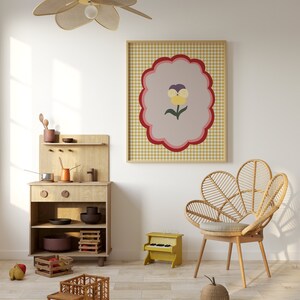 May include: A light wood play kitchen with a toy stove, oven, and shelves. A toy truck, a toy piano, and a wicker chair are in the room. A framed print with a yellow flower on a pink and white checkered background hangs on the wall.
