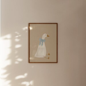 May include: A framed illustration of a white goose with a light blue bow sitting on a beige background.