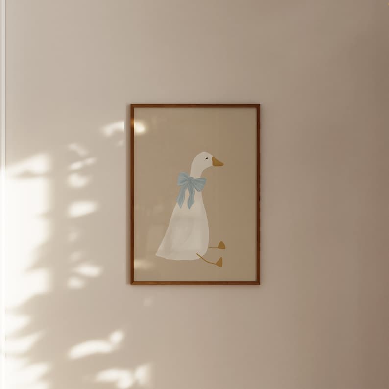 May include: A framed illustration of a white goose with a light blue bow sitting on a beige background.