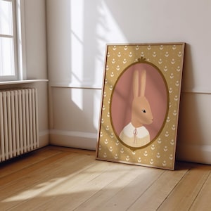 May include: A framed illustration of a brown rabbit wearing a yellow and white dress, with a pink background and a gold frame. The frame is surrounded by a yellow and white floral pattern.