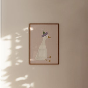 May include: A framed illustration of a white goose wearing a purple flower on its head. The goose is sitting down with its feet tucked under its body. The background is a light pink color.