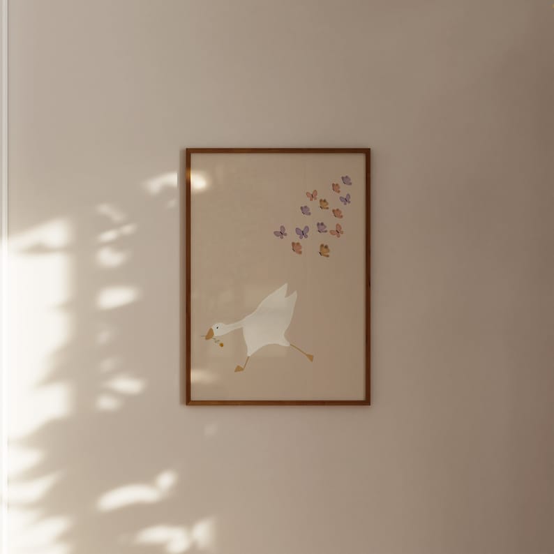 May include: A framed print of a white goose with a brown twig in its beak, flying towards a flock of purple and orange butterflies. The print has a light brown background and a wooden frame.