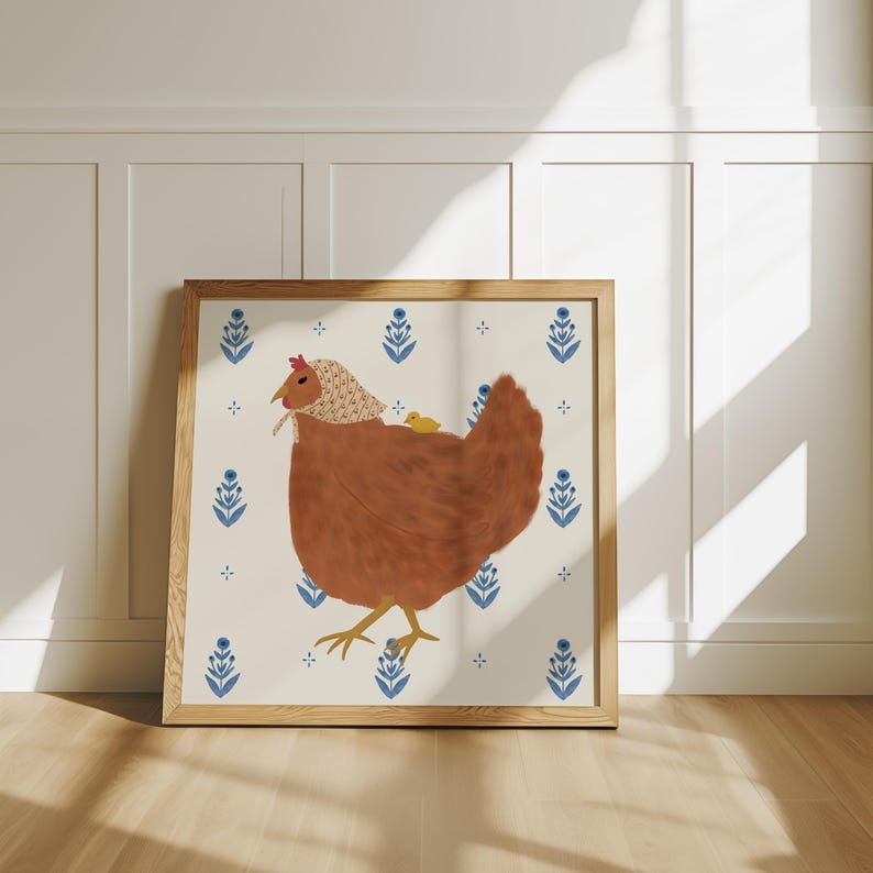 Puede incluir: Una ilustraci&oacute;n enmarcada de una gallina marr&oacute;n con un pollito amarillo en la espalda. La gallina lleva una capucha blanca y roja. El fondo es blanco con un patr&oacute;n floral azul y blanco.