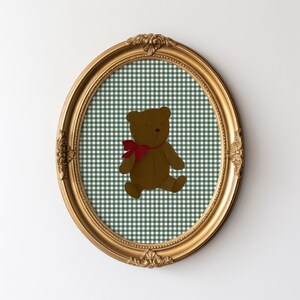 May include: A gold oval frame with a green and white gingham pattern and a brown teddy bear with a red bow.