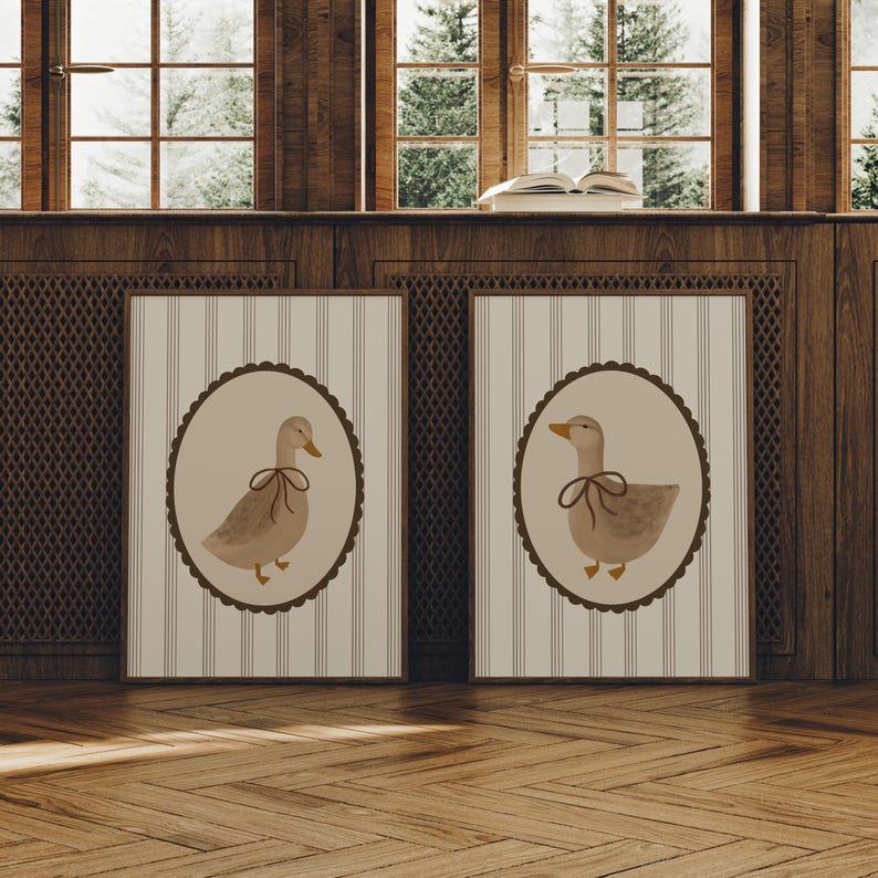 May include: Two framed prints with a striped background and a brown oval frame. Each frame contains a watercolor illustration of a duck with a brown ribbon around its neck.
