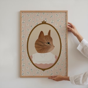 Pode incluir: Uma impress&atilde;o emoldurada de um gato vestindo um vestido rosa e um colar branco, com um fundo de padr&atilde;o floral.
