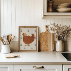 Puede incluir: Una impresi&oacute;n enmarcada de una gallina marr&oacute;n con un pico amarillo y un fondo estampado en azul y blanco. La impresi&oacute;n est&aacute; colgada en una pared blanca en un ambiente de cocina.