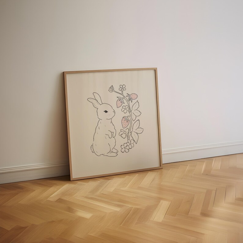 May include: A framed print of a white rabbit standing next to a pink and green strawberry plant with leaves and flowers. The print is on a cream-colored background.