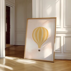 May include: A framed print of a yellow and white striped hot air balloon against a pink and white background. The balloon is floating in the sky with clouds.