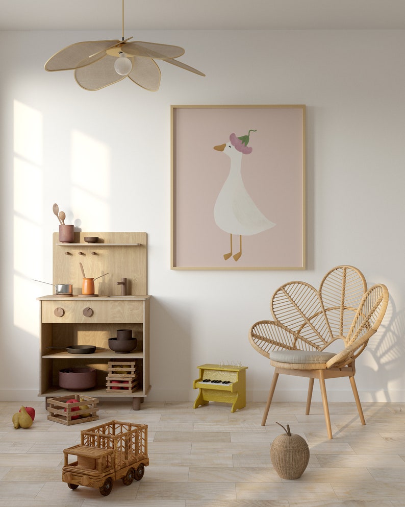 May include: A light wood play kitchen with a toy stove, shelves, and a wooden truck. A wicker chair with a light brown cushion sits in front of a framed print of a white goose wearing a pink flower on its head. A yellow toy piano sits on the floor.